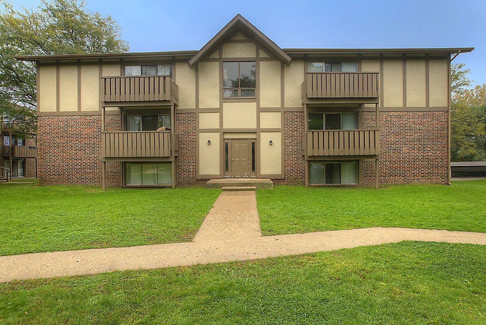 A residential apartment building with a well-maintained lawn and a pathway for easy access to the front door.